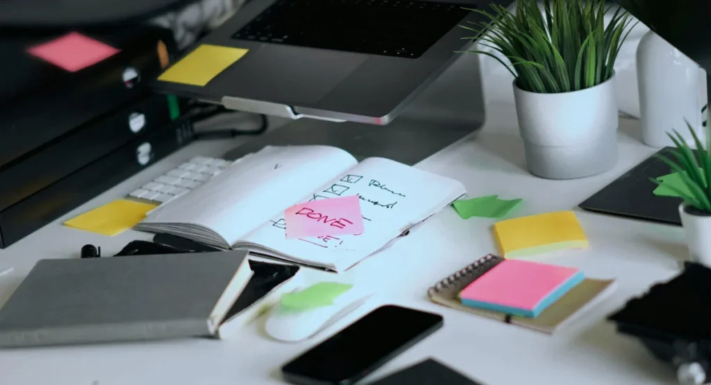 Image of a notebook, phones, and laptop with a lot of sticky notes on them